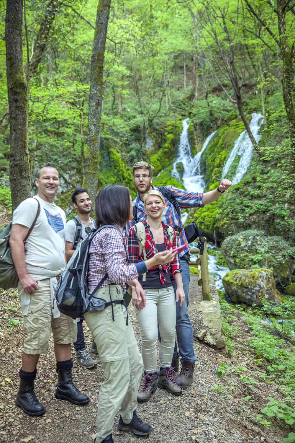 Lush forest waterfall hike with diverse group of travelers exploring nature and adventure outdoor destinations.