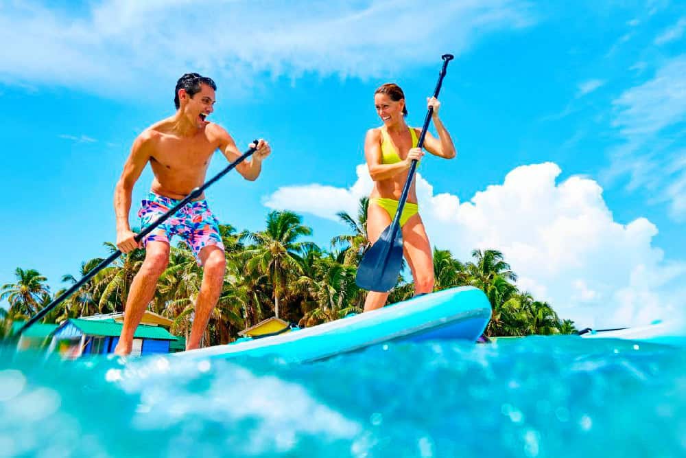 anniversaries-img-02 Adventure-loving couple enjoying paddleboarding at a tropical beach, perfect for exotic destinations and travel experiences.