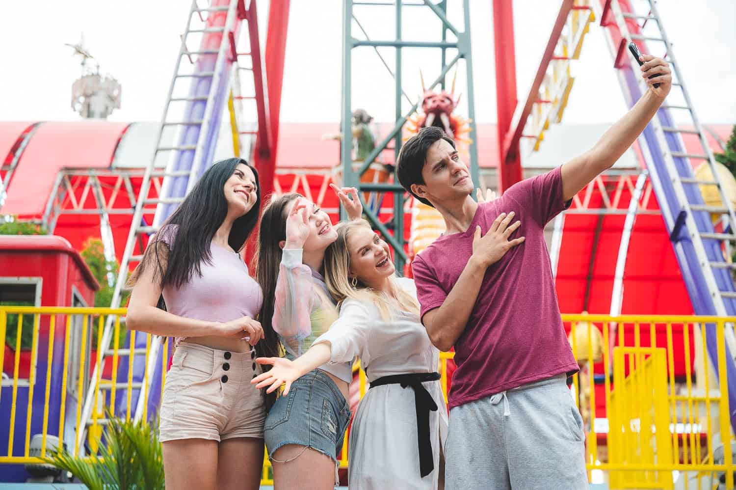 Bright group of friends taking a selfie at an amusement park with colorful rides, enjoying fun travel experiences and adventures for memorable vacation moments.
