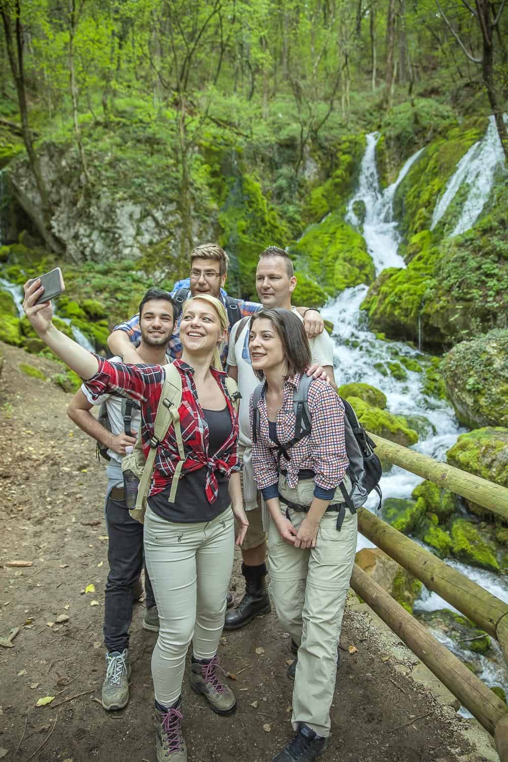 Waterfall hiking group adventure in lush forest, sustainable travel, outdoor exploration, eco-friendly tourism, scenic nature tour in green woodland setting.