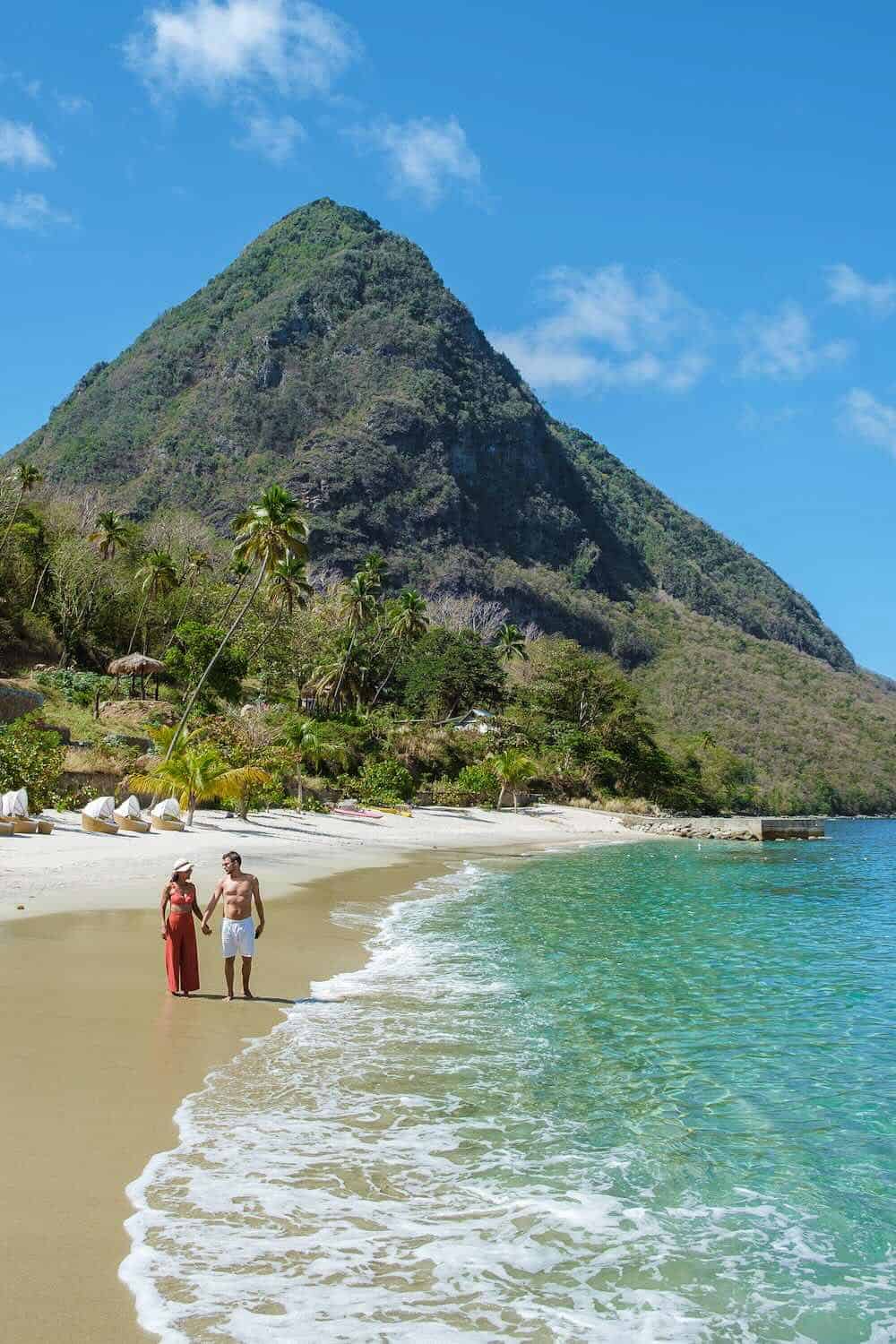 Exotic tropical beach with lush green mountain, clear turquoise waters, and couple walking hand in hand, perfect for luxury destination wedding, honeymoon, and travel photography.