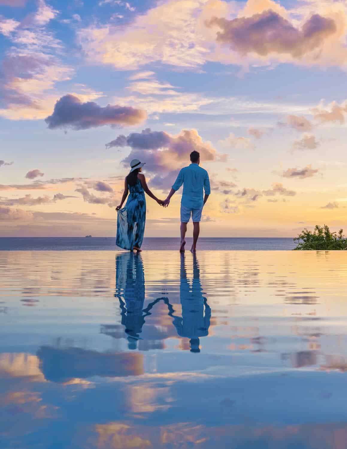 Romantic couple holding hands at sunset on a tropical beach, perfect destination wedding or honeymoon, beautiful ocean view with colorful sky, travel in paradise, I Do Destinations by vivid.
