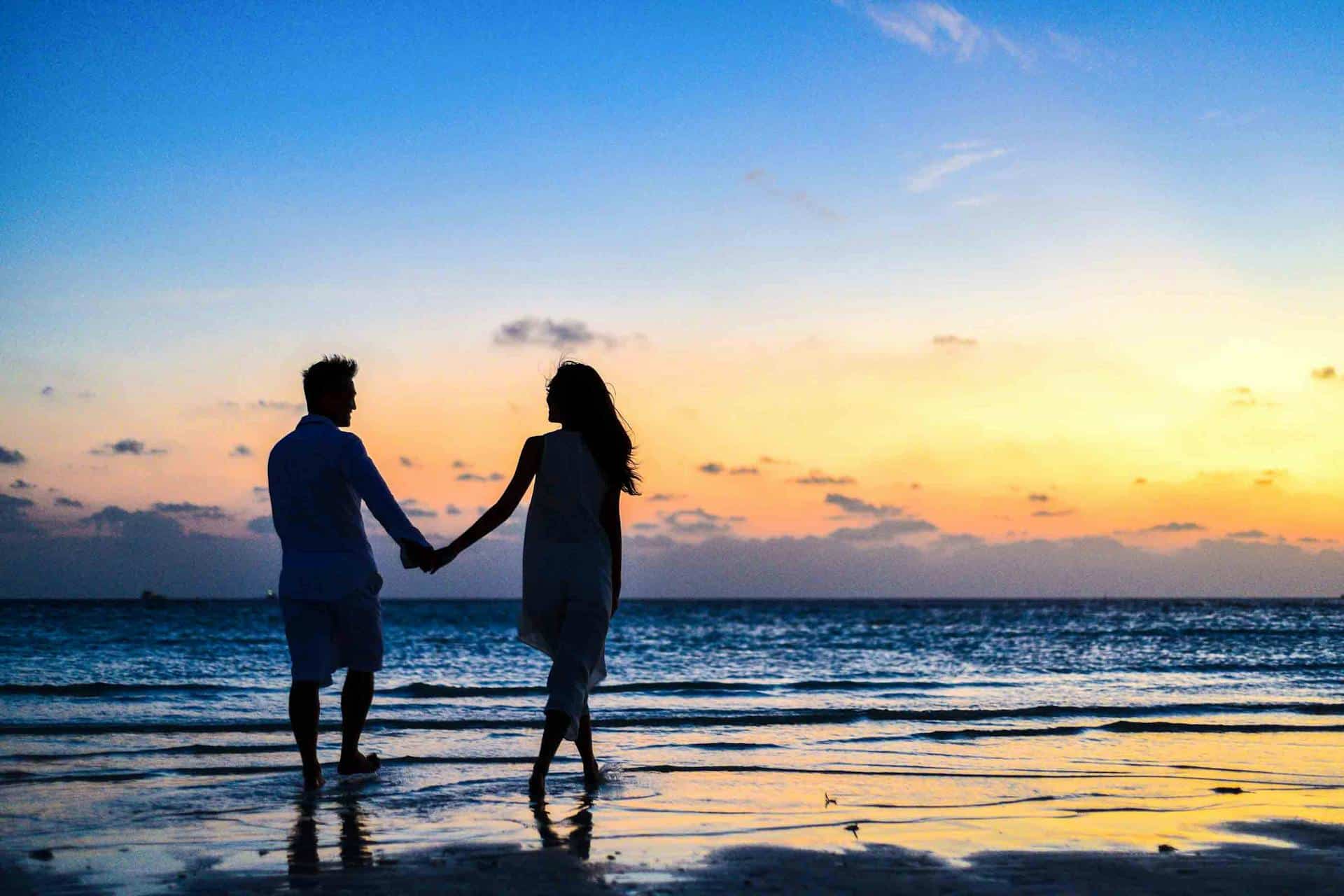 Romantic couple holding hands at sunset on the beach, perfect for wedding and honeymoon destination content.