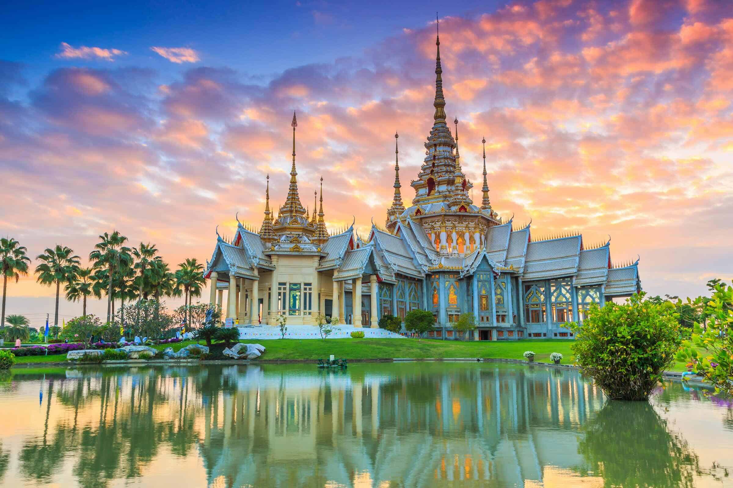anniversaries-img-02 Colorful Thai temple at sunset with vibrant sky, reflecting in a serene pond, showcasing Southeast Asia travel destinations and cultural landmarks.