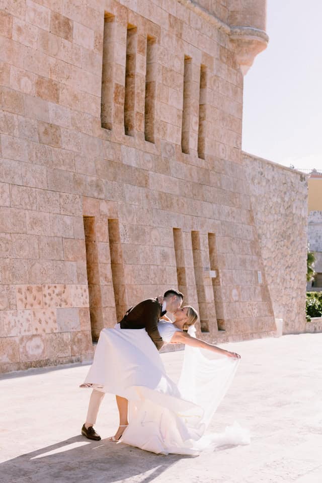 Elegant couple dancing outdoors in front of historic stone building, showcasing romantic destination wedding photography.