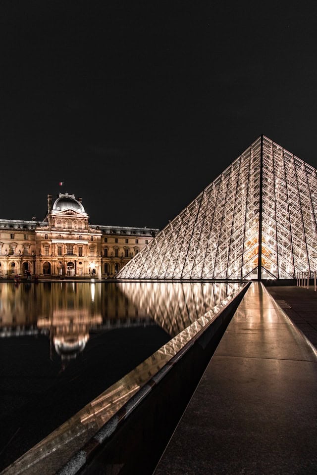 Gorgeous nighttime view of the Louvre Pyramid and historic palace in Paris, France, showcasing iconic travel destinations and luxury travel experiences.