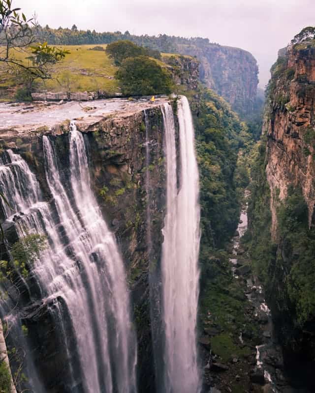 Majestic waterfall cascading over steep cliffs in lush green canyon, surrounded by dense forest and rocky terrain, showcasing breathtaking natural scenery and adventure travel destinations.