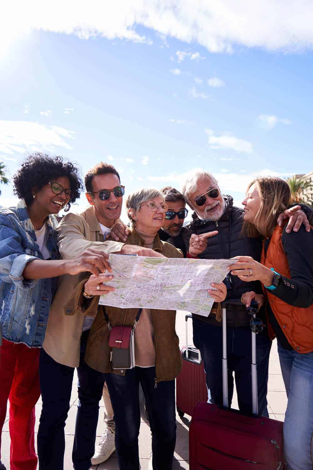Diverse group of travelers looking at a map outdoors, planning their journey on a sunny day.